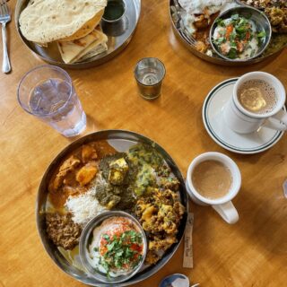 Silver dish full of Indian food on a wooden table with water and mugs of chai.