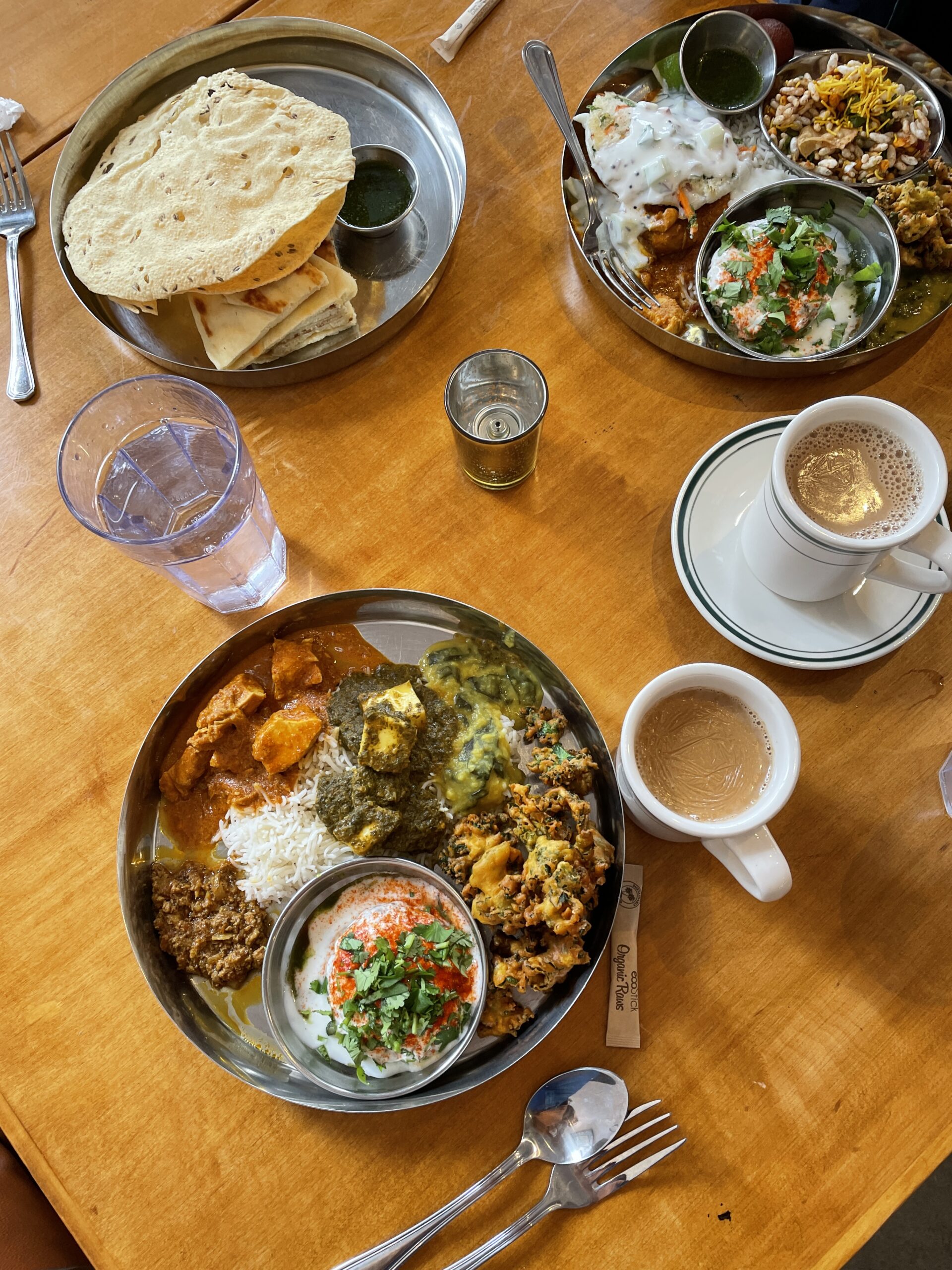 Silver dish full of Indian food on a wooden table with water and mugs of chai.