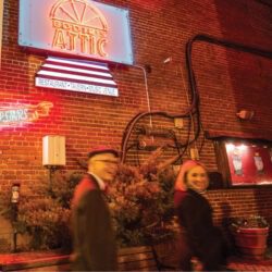 Couple walks past Eddie's Attic neon sign at night