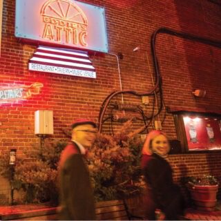 Couple Walks Past Eddie's Attic Neon Sign At Night