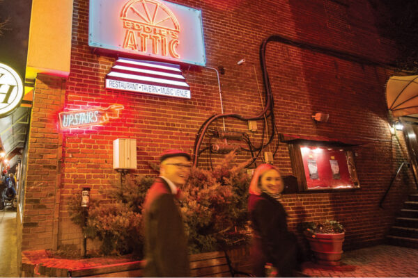 Couple walks past Eddie's Attic neon sign at night