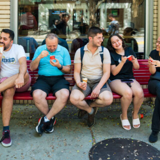 Group of adults sit on red bench eating ice cream.
