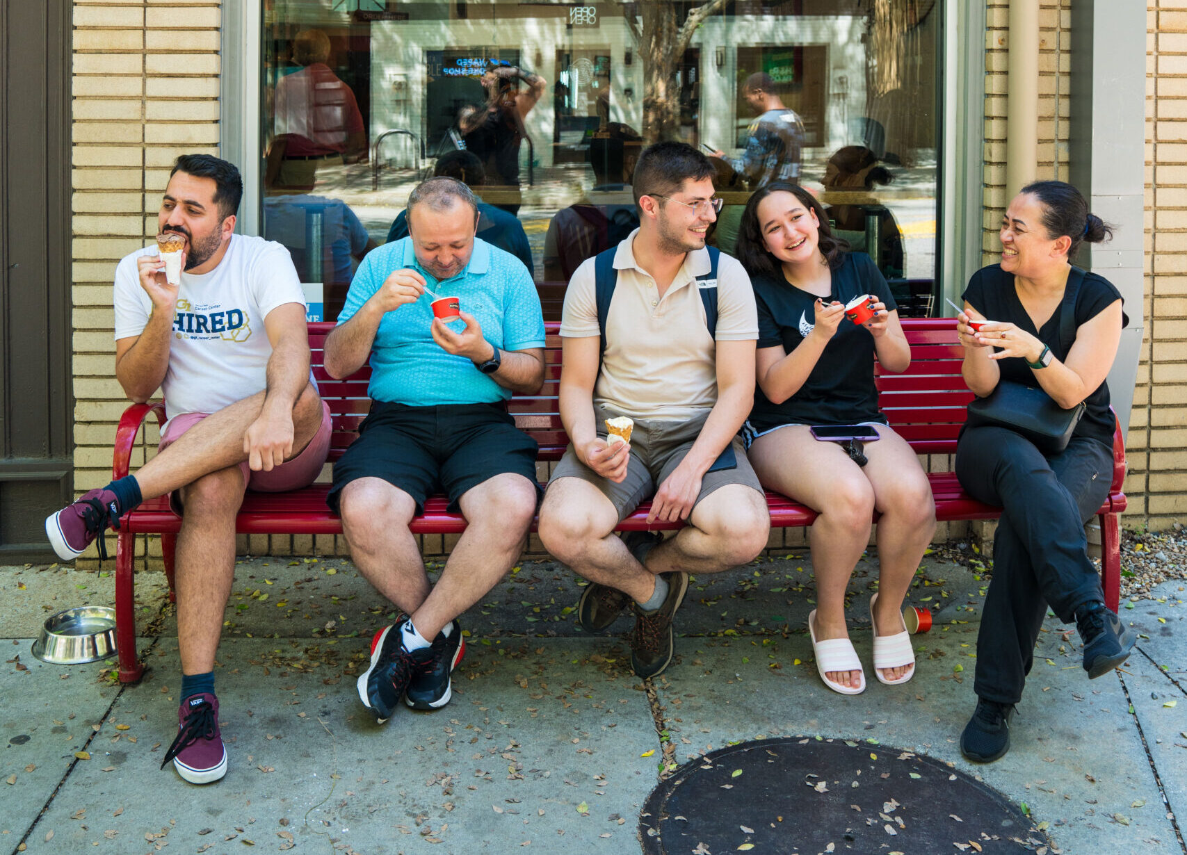 Group of adults sit on red bench eating ice cream.