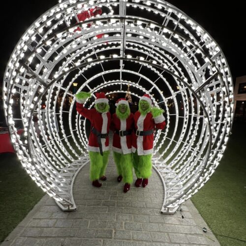 three bright-green "Grinches" with Santa suits inside ornament holiday light display