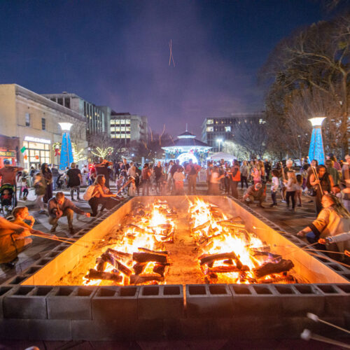 crowds of people on the downtown plaza roasting marshmallows at large bonfire