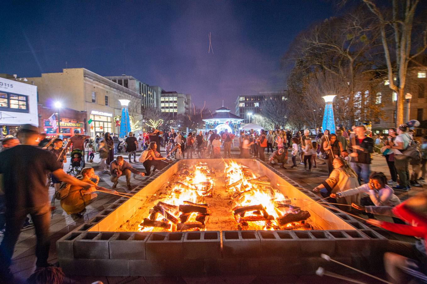 crowds of people on the downtown plaza roasting marshmallows at large bonfire