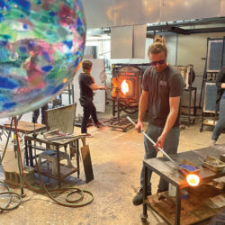 Artists shaping molten glass inside a glassblowing workshop.