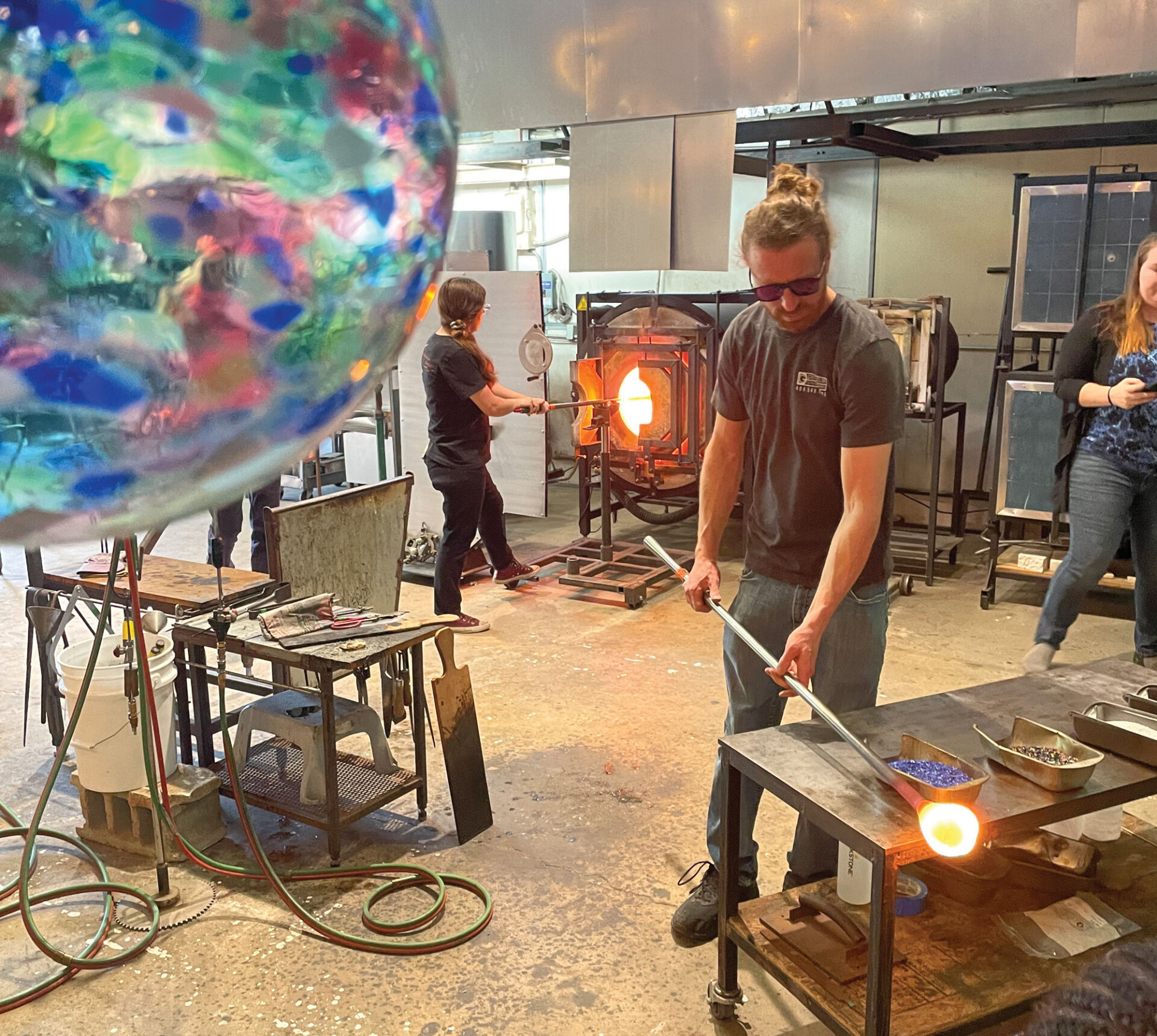Artists shaping molten glass inside a glassblowing workshop.