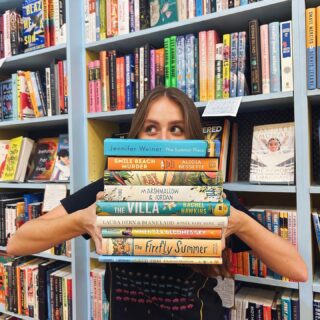 Woman holds stack of books at Little Shop of Stories