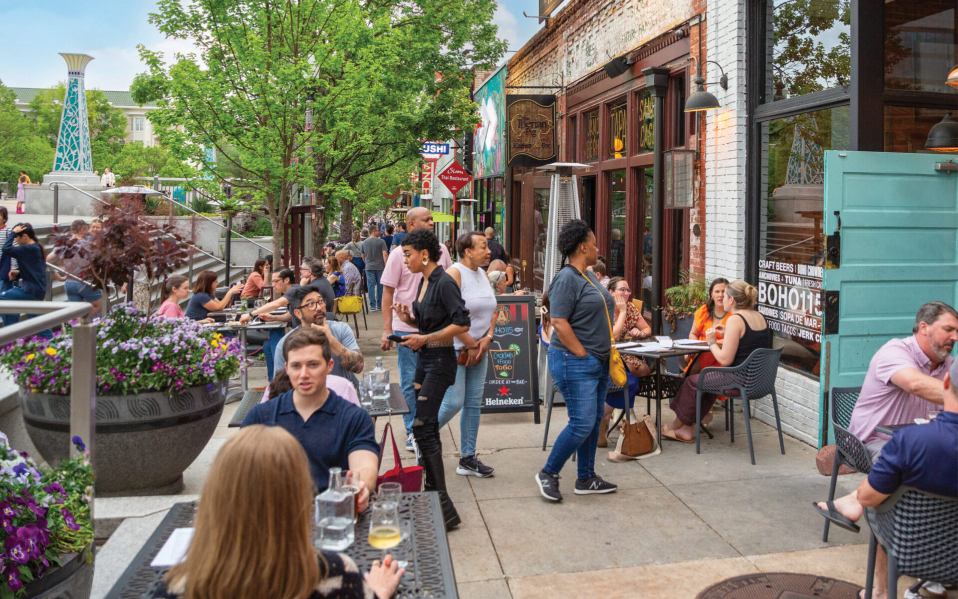 Tables full of people line the wide pedestrian sidewalk in front of restaurants along the Decatur Square.